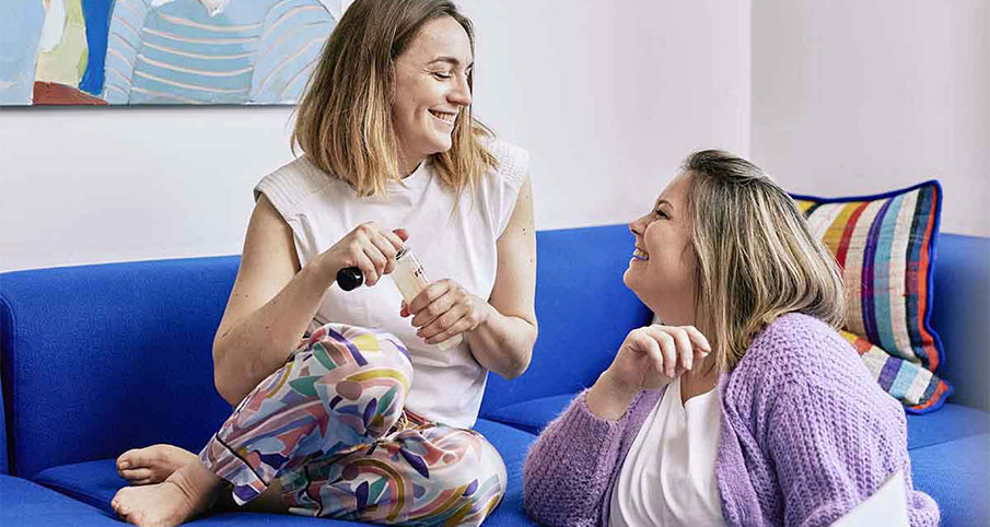 Une femme souriante tient un shampoing Formy dans ses mains et regarde une autre femme souriante