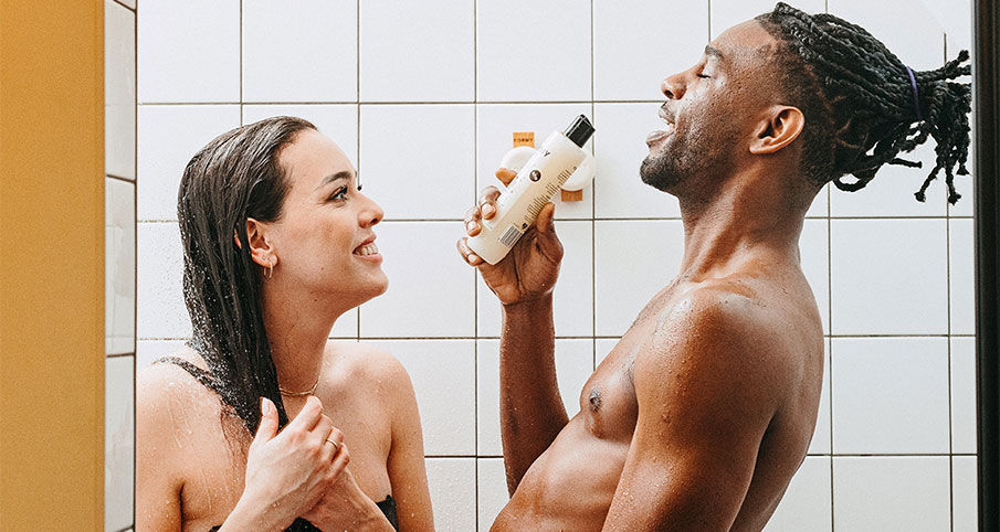 Une femme et une homme qui prennent une douche et l'homme tient une bouteille de shampoing