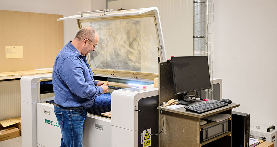 Un homme est en train de travailler sur une machine de gravure inspecte un morceau de bois avec le mot Formy