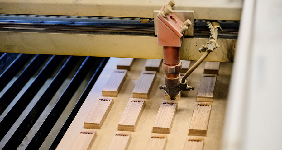 Machine en train de graver le mot "Formy" dans chaque morceau de bois