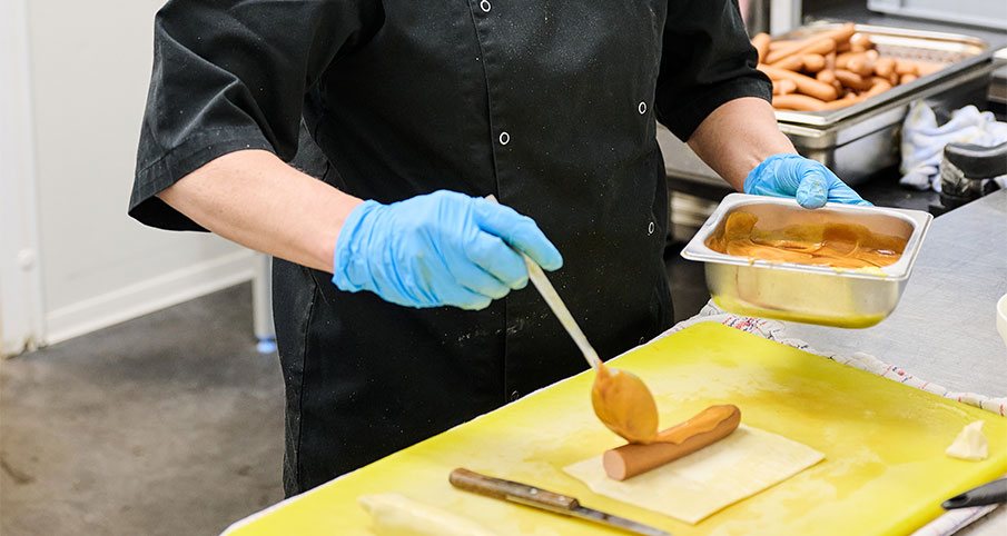 Un cuisinier en train d'ajouter de la sauce sur une saucisse